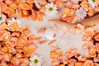 bombe de bain blanche qui se dissous dans un bain avec des pétales de fleur orange et des fleurs entière blanche autour